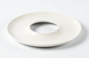  A modern porcelain plate by Arabia AB with a unique donut-like shape, featuring a central hole, displayed on a light background. The creamy white color of the glazed porcelain reflects gentle light, creating soft shadow around the plate.