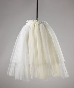  A Jonas Bohlin-designed lamp with a skirt-shaped white tulle shade that softly diffuses light, suspended against a neutral background.