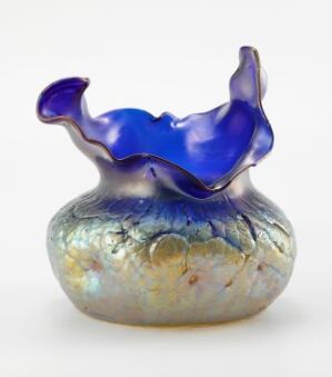  Decorative iridescent glass vase with a wavy cobalt blue rim transitioning into a body with swirls of mother-of-pearl, lavender, and creamy yellow colors.