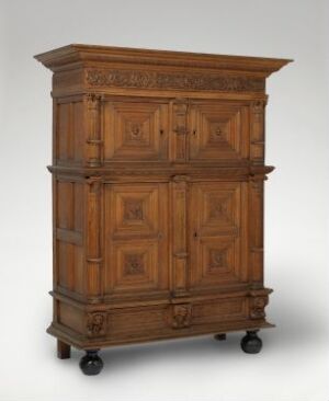  A traditional wooden cabinet on casters with intricate geometric paneling on two sets of doors, one above the other, in a warm medium-brown tone against a light gray background.