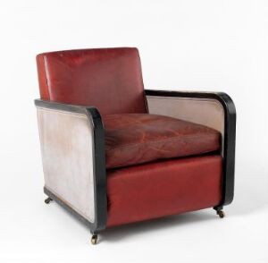  A vintage modernist armchair with deep red leather upholstery for the seat and backrest, cream hide on the outer sides, and a dark frame, set against a plain background, equipped with brass casters.