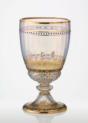  An intricately designed glass goblet with a golden rim, a band depicting a traditional landscape scene, and multicolored jeweled dots below the scene. The goblet has a short stem and a wide base and is positioned against a light grey background.