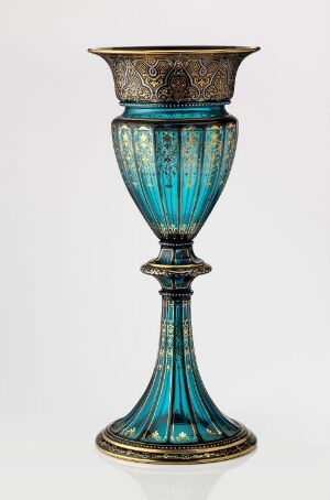  An ornate turquoise goblet with intricate gold embellishments on the rim and base, set against a light background.