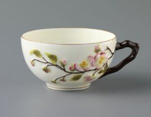  A feldspar porcelain cup titled "Rosengren" by an unknown artist, featuring a light cream color with a floral design of pastel pink blossoms and olive green branches, a rich brown handle, and possible gold accents, set against a neutral grey background.