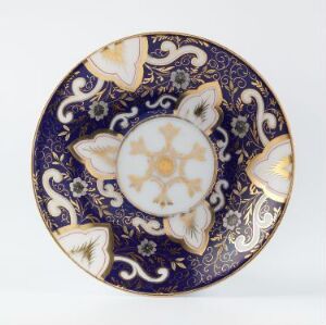  A decorative porcelain plate with rich royal blue and gold overglaze decoration including symmetrical motifs and a centered star-like pattern, designed by Porsgrunds Porselænsfabrik AS. The plate features detailed white and gold patterns on a deep blue background, reflecting an elegant and luxurious design.