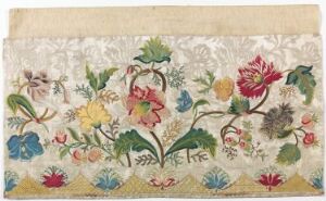 
 An embroidered textile with a cream background showcasing a colorful and detailed floral design, featuring a variety of flowers in rich hues of pinks, blues, greens, and purples, indicative of handcrafted artistry.