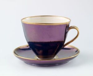  A teacup and saucer set with a gradient of deep purple to light mauve colors, both edged with a fine gold trim, against a neutral light grey background.