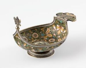  An ornate, historic-style gravy boat-like object with elaborate multicolored floral and botanical decorations over a dark metallic background, featuring a curling handle with a detailed figure at the crest, all set on a small, decorated base. Artist name and title unknown.