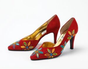  A pair of elegant red high-heeled shoes with golden interior lining and colorful floral embroidery featuring blue, red, orange, and green details on the sides.