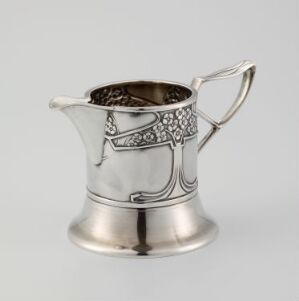  An Art Nouveau style small silver jug with an openwork leaf design on one side and a gracefully curved handle. The jug exhibits a polished surface with delicately incorporated darker tones in the vine-like pattern.