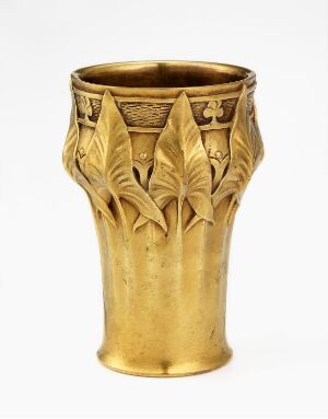  A tapered gold cup with embossed leaf patterns, glowing with a warm metallic sheen against a neutral background. The intricate craftsmanship suggests a decorative or ceremonial use. Artist name and title remain unknown.