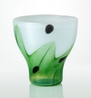  A hand-blown glass vessel designed by Kari Ulleberg with a milky white background featuring abstract green leaf-like shapes and scattered black dots, indicative of seeds or berries, creating an artistic design on the tableware.