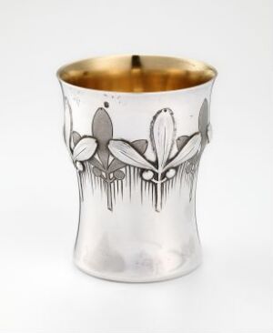  A decorative metal cup with a flared opening and a gold-tone interior. It features an etched Art Nouveau-style floral design on a silver exterior set against an off-white background. Artistname and title are unknown.