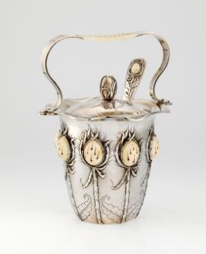  An ornate silver ice pail with golden medallions and curvilinear flourishes, featuring a scrolled handle and a decorative border below the rim.