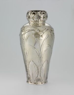  A metallic-sheen vase with an embossed design featuring two stylized women's heads at the neck, forming a rim, with a continuous pattern of flowers and flowing stems carved into the body of the vase.