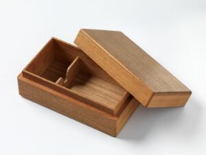  An open wooden box with a partition inside, creating two compartments, set against a light grey background. The box is open with the lid placed askew, showcasing the warm brown wood grain. Artist name and title are unknown.