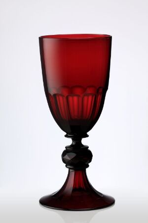  A translucent red glass goblet with a textured bowl and a decorative stem, set against a plain light background.