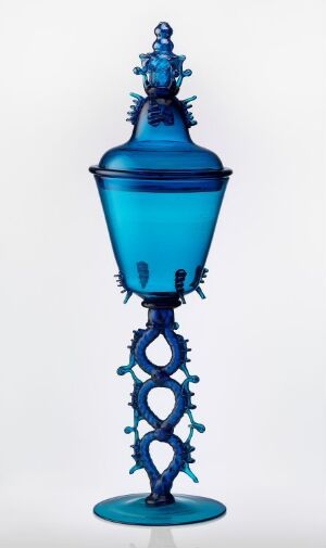  An ornate blue glass object with a bulbous body, intricate stem, and decorative lid set against a light background.