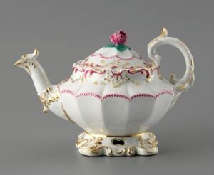  An ornately designed white teapot with pink and gold accents, baroque-style gilded feet, a sculpted spout, and a floral finial in pink and green, against a gray background.