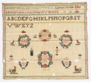  An antique cross-stitched sampler with the alphabet and numbers at the top, surrounded by symmetrically arranged floral motifs and pastoral scenes in red, green, and pink hues on a natural linen background. The edges show signs of fraying, indicating the piece's age.