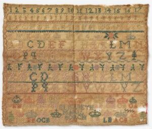  An antique-looking needlework sampler with rows of numbers, letters, and colorful motifs on light beige fabric, showing signs of age and wear.