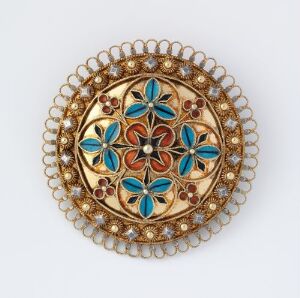  A luxurious circular brooch with symmetrical gold, deep blue, turquoise, and red-brown enamel designs, featuring a central flower motif and an intricate fringe of interlocking gold circles.