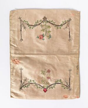  A vintage square piece of fabric with an off-white background, showing signs of aging, adorned with symmetrical embroidered garland designs depicting green vines, red roses, and small pastel flowers on the upper and lower halves.