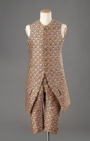  A sleeveless, asymmetrical dress with a geometric diamond pattern in shades of pink, cream, and brown displayed on a mannequin against a gray background.