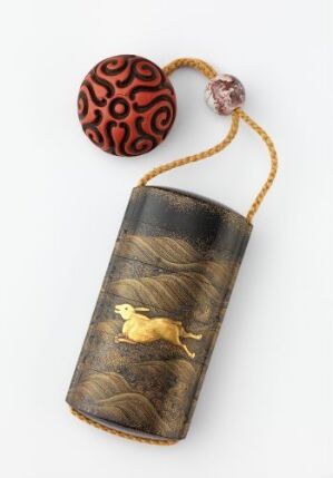  A dark-colored etui with a golden bird inlay, attached to a beaded cord with a prominent red and black patterned bead, against a light greyish-white background.