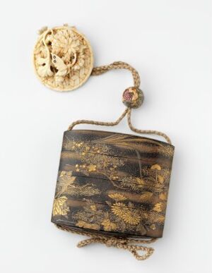  A traditional Japanese inro with gold detailing on a black lacquer background, attached to an intricately carved ivory-colored netsuke and ojime bead.