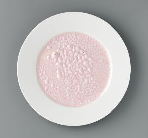  A porcelain artwork "Monokromer" by Heidi Bjørgan, featuring a textured pink glazed center surrounded by a smooth white outer rim, placed on a neutral gray surface.