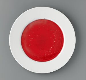  "Monokromer" by Heidi Bjørgan, a round porcelain plate with a vibrant red glazed center contrasted by the surrounding matte white surface.