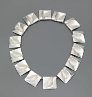  A sculptural silver necklace by Lapponia Jewelry Oy displayed on a light grey background, consisting of geometrically cut, polished silver segments linked to form a complete circle, demonstrating modern design and expert craftsmanship.