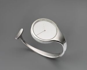  A minimalistic stainless steel and glass wristwatch designed by Torun Bülow-Hübe, with a curving band and a simple white dial with black hands, set against a grey background.