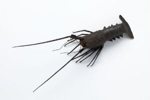  A sculpted object resembling a robotic insect with a hex-headed screw for a head, barbed cylindrical body, wire-like antennae, and metallic legs against a light gray background. The colors are mainly dark browns and blacks with metallic highlights.