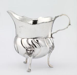  A silver cream jug titled "Fløtemugge" by Jørgen Jørgensen Leman. The jug is set against a neutral background, showing a reflective surface with wavy contours and a decorative creature's face on the central leg.