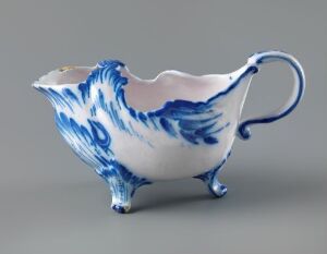  A porcelain sauce boat with blue floral patterns on a white background, featuring an elegant handle and flared rim for pouring. The artist's name and title of the work are unknown.