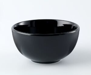  A glossy black ceramic bowl designed by Kaj Franck with a simple, elegant form, showcasing a lustrous finish against a neutral off-white background.