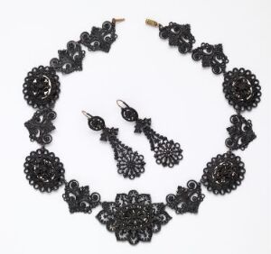  A black lace jewelry set against a light background, including an ornate floral-patterned necklace and matching dangling earrings, showcasing intricate details and vintage style. Artistname is unknown, and the title is also unknown.