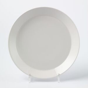  A creamy white, glazed round plate with a slightly raised edge, resting on a clear stand against a plain white background. Designed by Iittala.