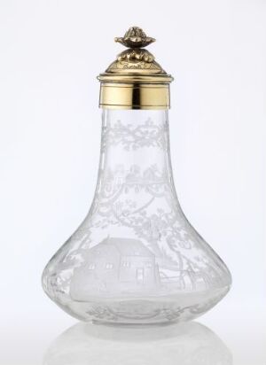  A decorative clear glass bottle with etched designs and a golden metal lid featuring an ornate finial, against an off-white background.