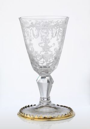  An ornate clear glass goblet with an etched design on the bowl and a golden rim around the base, set against a white background. Artist name and title are unknown.