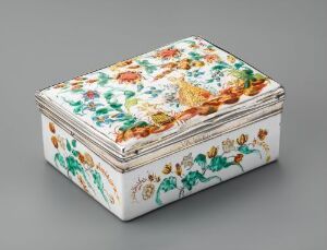  An intricately hand-painted porcelain box with a floral design in oranges, reds, yellows, and pinks on the lid, a leafy green pattern on its sides, and a blue and gold border, presented against a soft grey background.