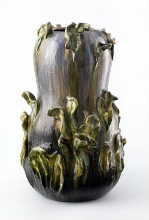  An ornate ceramic vase with a glossy dark grey to silver gradient finish and stylized green leaf-like protrusions cascading down its sides.