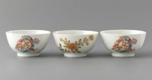  A set of three white porcelain bowls with intricate floral designs in various colors including deep pink, muted orange, soft yellow, and shades of green and blue, highlighted against a plain grey background.