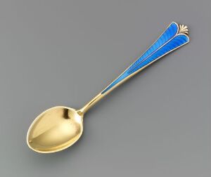  A gilded silver coffee spoon called "Mokkaskje" by David-Andersen, with a long handle featuring guilloche engraving under vibrant blue enamel, against a neutral background.