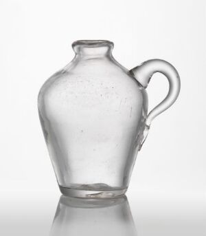  A small, slightly cloudy glass pitcher with a single curved handle against a white background, exhibiting a simple and classic design.