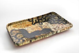  A rectangular ceramic dish called "Det svarte og oransje fatet" by Marit Tingleff, featuring abstract black patterns against a mottled orange, white, and yellow background with a pale border decorated with vertical black lines. The dish demonstrates a bold, artistic design with a rustic texture.