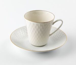  A delicately crafted feldspar porcelain cup with a quilted diamond relief pattern and a matching saucer trimmed with a fine gold band, designed by Eystein Sandnes against a plain white background.