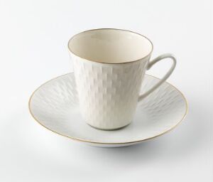  A high-quality cream-colored feldspar porcelain cup with a textured geometrical relief and a matching saucer, both edged with delicate gold accents, designed by Eystein Sandnes against a neutral background. The title of the piece is unknown.